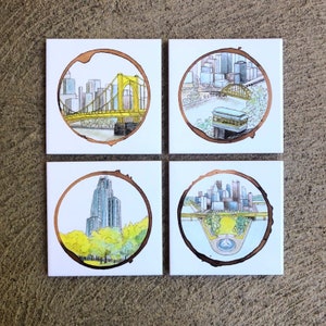 Pode incluir: Conjunto de quatro  apoios de copo de cer&acirc;mica com um design de anel de caf&eacute; castanho com ilustra&ccedil;&otilde;es de marcos de Pittsburgh. Os apoios de copo representam o horizonte da cidade, a ponte Roberto Clemente, o Duquesne Incline e a Catedral do Aprendizado.