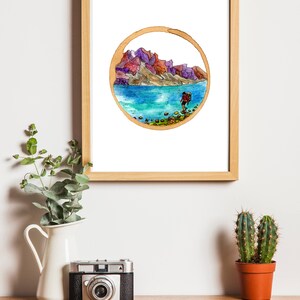 May include: A framed watercolor painting of a hiker walking along a rocky shore with mountains in the background. The painting is in a circular frame with a brown border.