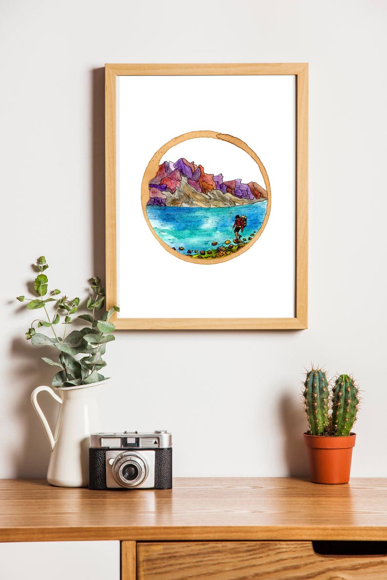May include: A framed watercolor painting of a hiker walking along a rocky shore with mountains in the background. The painting is in a circular frame with a brown border.