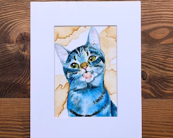 Puede incluir: Una pintura de acuarela de un gato atigrado azul con ojos verdes. El gato está mirando al espectador y tiene la lengua fuera. El fondo es de color marrón claro.