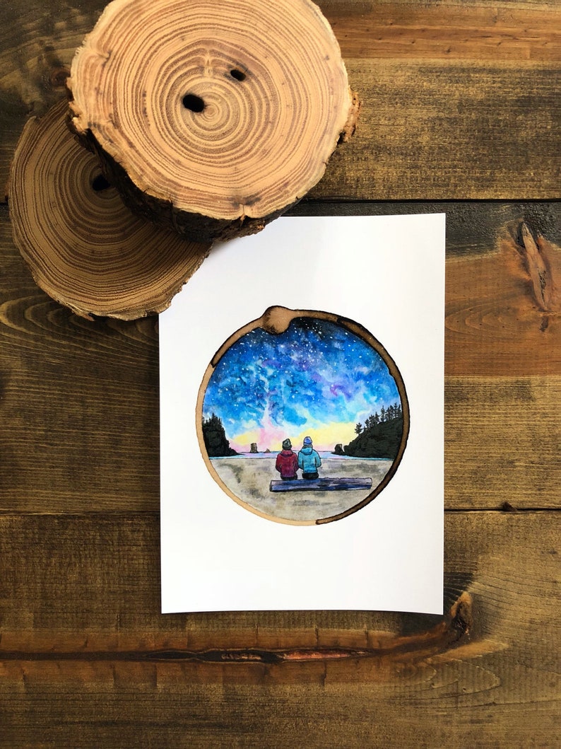 May include: A watercolor painting of two people sitting on a log, looking out at a starry night sky. The painting is framed in a round wooden circle.