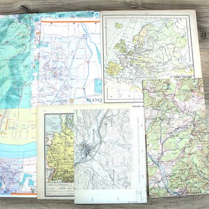 Op de afbeelding: Een verzameling vintage papieren kaarten van diverse geografische regio's, waaronder een politieke kaart van Europa, topografische kaarten met hoogtelijnen en gedetailleerde plattegronden met teksten zoals Blanq en Masevaux.