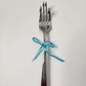 May include: A silver fork tied with a turquoise ribbon bow.