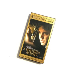 May include: A gold VHS tape case with a picture of Russell Crowe from the movie "A Beautiful Mind." The case has the text "4 Academy Awards Best Picture" and "The Awards Edition."