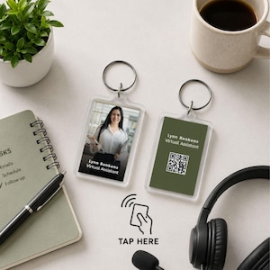 Puede incluir: Dos llaveros rectangulares de acrílico transparente con anillas metálicas. Uno muestra una fotografía con el texto Lynn Renkens Virtual Assistant. El otro tiene un fondo verde oliva, un código QR y el texto Lynn Renkens Virtual Assistant. Un icono con el texto TAP HERE se sitúa entre ambos.