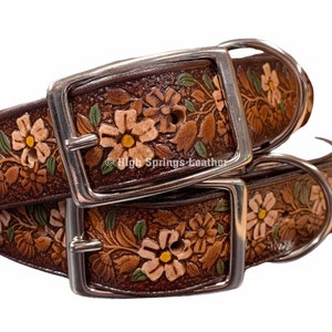 May include: Two brown leather dog collars with floral tooled designs. The collars have silver buckles and D-rings. The collars are stacked on top of each other.