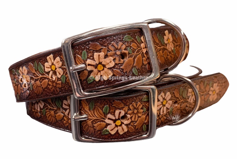 May include: Two brown leather dog collars with floral tooled designs. The collars have silver buckles and D-rings. The collars are stacked on top of each other.