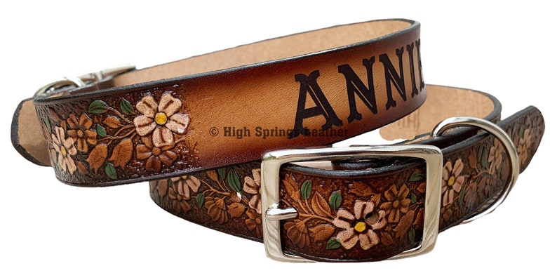 May include: Brown leather dog collar with a floral design and the name "ANNIE" embossed on the top. The collar has a silver buckle and a D-ring.