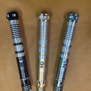 Puede incluir: Tres empu&ntilde;aduras de sable l&aacute;ser en diferentes colores: negro, dorado y plateado. Cada empu&ntilde;adura tiene un dise&ntilde;o texturizado y un bot&oacute;n en el lateral.