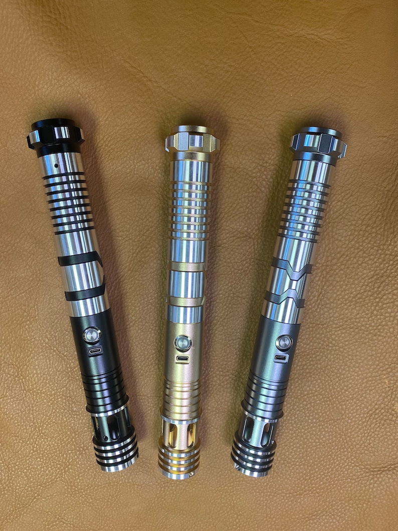 Puede incluir: Tres empu&ntilde;aduras de sable l&aacute;ser en diferentes colores: negro, dorado y plateado. Cada empu&ntilde;adura tiene un dise&ntilde;o texturizado y un bot&oacute;n en el lateral.