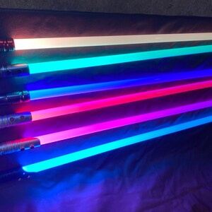 Puede incluir: Cinco empu&ntilde;aduras de sable l&aacute;ser con hojas de diferentes colores. Las hojas est&aacute;n iluminadas en blanco, azul verdoso, azul, rosa y azul claro.