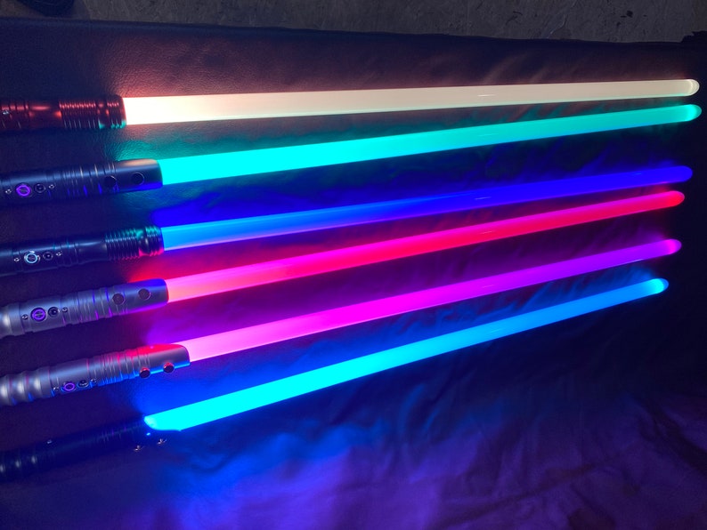 Puede incluir: Cinco empu&ntilde;aduras de sable l&aacute;ser con hojas de diferentes colores. Las hojas est&aacute;n iluminadas en blanco, azul verdoso, azul, rosa y azul claro.