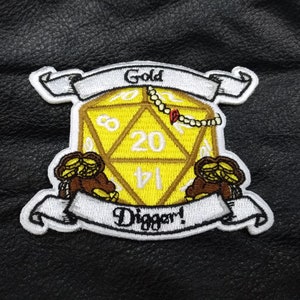 May include: Embroidered patch featuring a yellow D20 die with the number 20 prominently displayed. The patch includes the words "Gold Digger!" and "Gold" on white banners, along with a gold chain and two treasure chests.