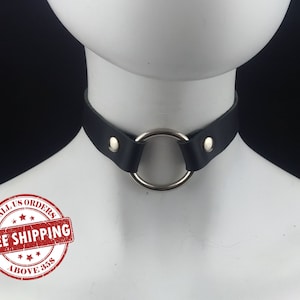 May include: Black leather choker with a silver ring. The choker has two silver studs on each side. The image has a red stamp that says "On all US orders Free Shipping Above $35"
