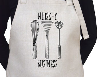 May include: A white linen apron with a black print of three whisks and the text "WHISK-Y BUSINESS".
