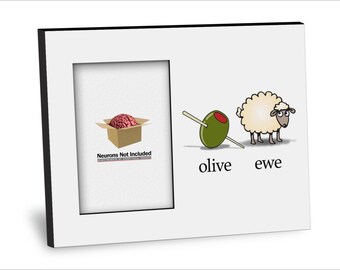 May include: A white picture frame with a black border. The frame contains a cartoon image of a brain in a box with the text "Neurons Not Included" and a cartoon image of an olive and a sheep with the text "olive" and "ewe".