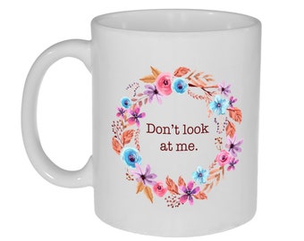 May include: White ceramic mug with a floral wreath design in shades of pink, blue, and purple. The text "Don't look at me." is printed in brown inside the wreath.