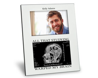 May include: A white picture frame with a black and white image of a brain scan. The text "All that studying warped my brain" is printed below the image. The frame has a photo of a man smiling in the top section.