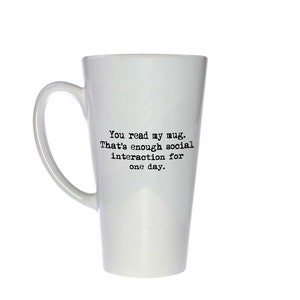Op de afbeelding: Een witte keramische latte-mok met zwarte tekst die "You read my mug. That's enough social interaction for one day." zegt.