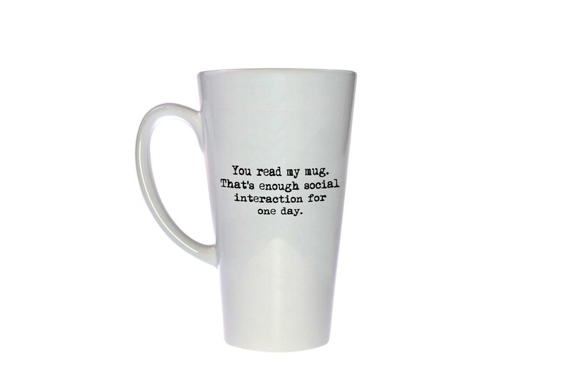 Op de afbeelding: Een witte keramische latte-mok met zwarte tekst die "You read my mug. That's enough social interaction for one day." zegt.