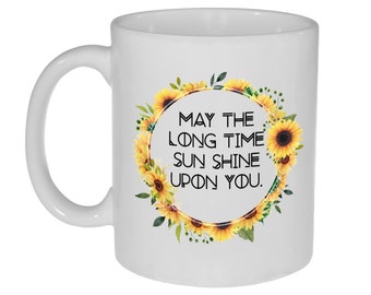 May include: White ceramic coffee mug with a sunflower wreath design and the text "May the long time sun shine upon you."
