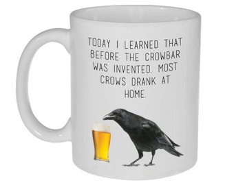 May include: White ceramic mug with a black crow drinking from a glass of beer. The mug has the text "TODAY I LEARNED THAT BEFORE THE CROWBAR WAS INVENTED, MOST CROWS DRANK AT HOME."
