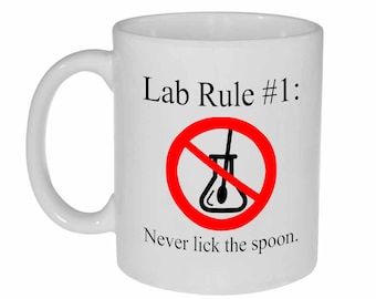 May include: White ceramic mug with a red circle and a diagonal line through it. The circle contains a black and white illustration of a beaker with a stirring rod. The text "Lab Rule #1: Never lick the spoon." is printed on the mug.