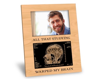 May include: A wooden picture frame with a photo of a man smiling. The frame has the text "ALL THAT STUDYING WARPED MY BRAIN" and a black and white image of a brain scan with the word "PROF" inside.