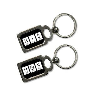 May include: Two silver keychains with black rectangular tags. The tags have the chemical symbols for hydrogen, erbium, and sulfur, spelling out "His" and "Hers".