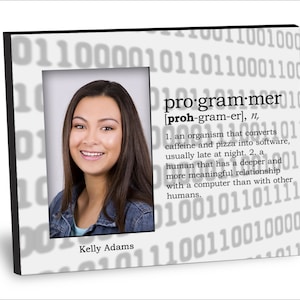 May include: A white picture frame with a black border. The frame has a photo of a woman with brown hair and a black and blue denim jacket. The frame has a white background with a gray pattern of binary code. The text "programmer" is written in black with a definition below. The name "Kelly Adams" is written below the photo.