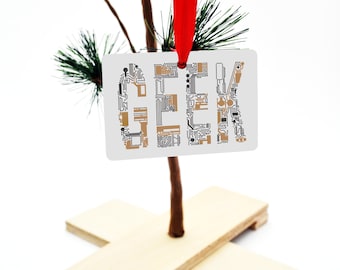 May include: A white ornament with the word "GEEK" printed in black with a brown circuit board pattern. The ornament is hanging from a red ribbon on a small artificial pine tree.