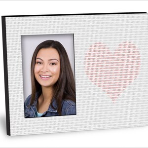 May include: A black picture frame with a white background and a red heart shape made of binary code. The frame has a photo of a young woman with long brown hair smiling at the camera.