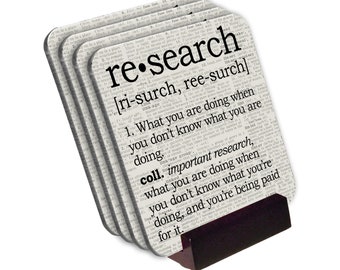 May include: Set of four white coasters with a black and white dictionary definition of the word "research". The coasters are stacked and leaning against a black stand.