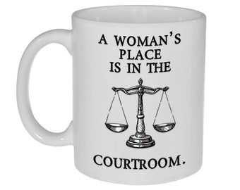 May include: White ceramic coffee mug with a black graphic that reads "A woman's place is in the courtroom." The graphic also includes a black and white illustration of a scale.