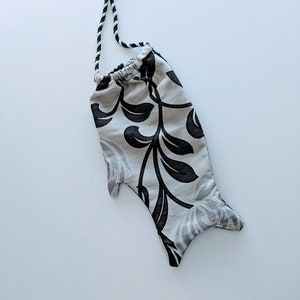 May include: A white and black patterned drawstring bag shaped like a fish. The bag has a black and white rope handle.