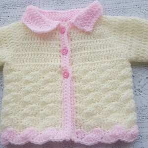 Könnte beinhalten: Eine gehäkelte Babyjacke in Gelb und Rosa mit Knöpfen und einem Kragen.