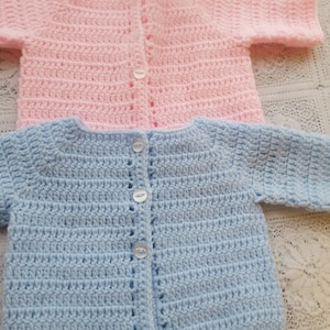 May include: Two crocheted baby cardigans, one in pink and one in blue, with button fastenings.