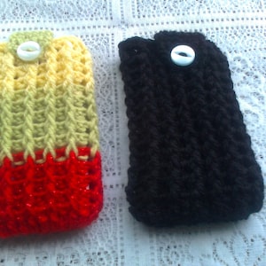 May include: Two crocheted phone cases, one in red, yellow, and green, and the other in black. Both cases have a white button.