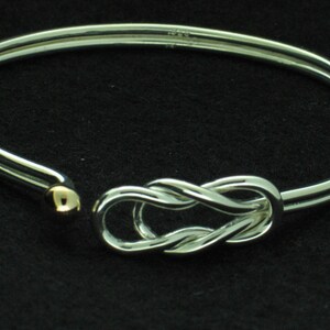 May include: A silver bangle bracelet with a gold accent and a knot design.
