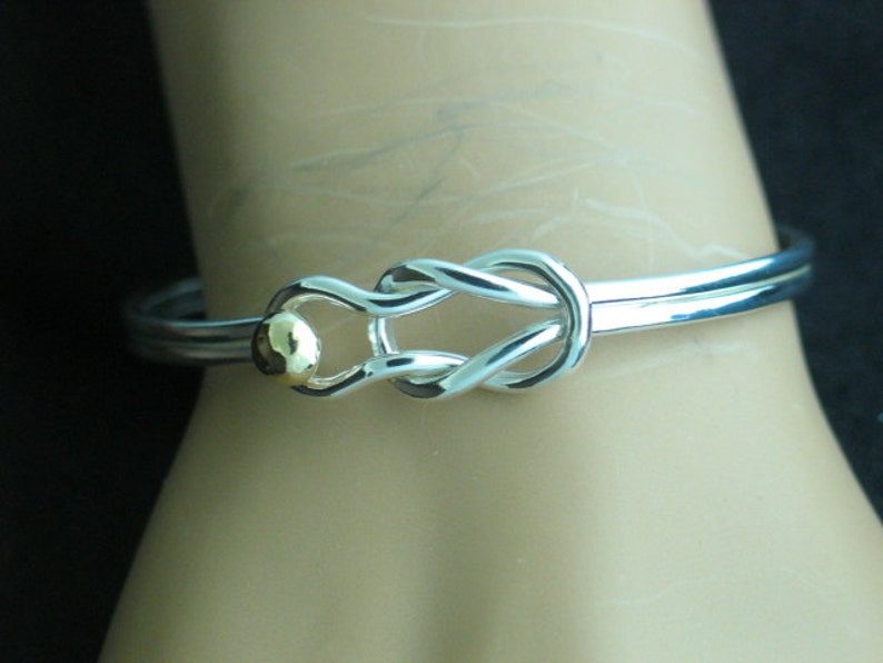 May include: A silver bangle bracelet with a knot design and a small gold bead accent.