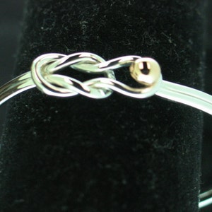 May include: A silver bangle bracelet with a knot design and a small gold bead accent.