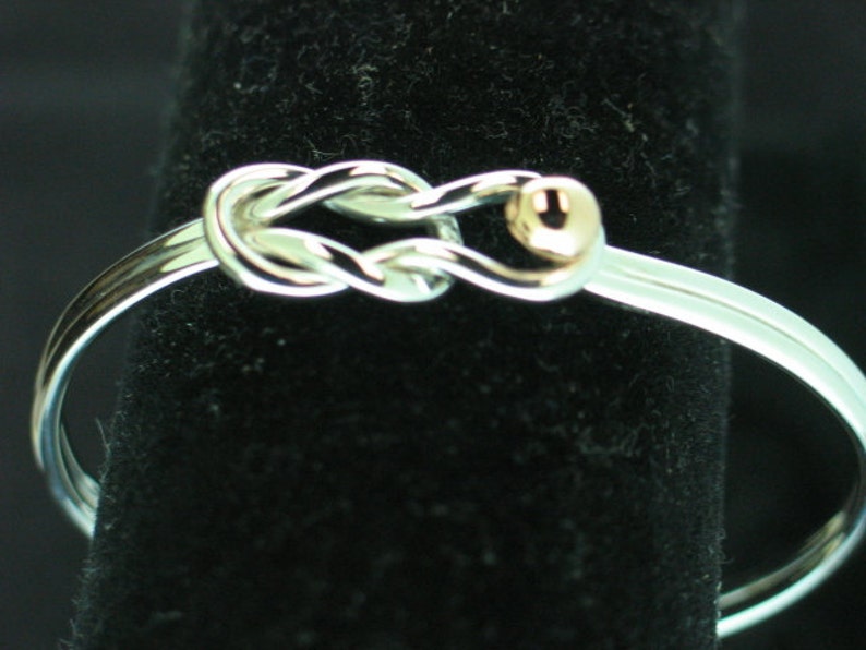 May include: A silver bangle bracelet with a knot design and a small gold bead accent.