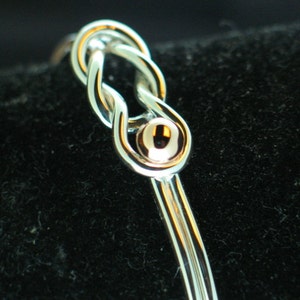 May include: A silver bangle bracelet with a gold knot design and a small gold bead accent.