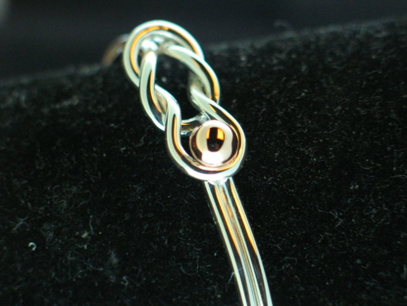 May include: A silver bangle bracelet with a gold knot design and a small gold bead accent.