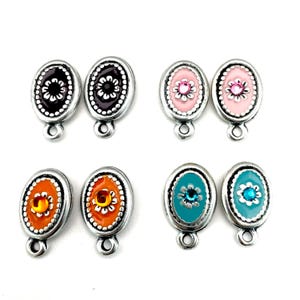 May include: Eight oval jewellery findings in a variety of colours. Each finding has a silver-coloured frame with a decorative centre. The centres feature black, pink, orange, and teal enamel with floral or gem-like details. Each finding has a loop at the bottom.