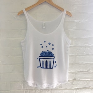 K&ouml;nnte beinhalten: Wei&szlig;es Tanktop mit einer blauen Illustration eines Korbes, der &uuml;berquillt mit Blaubeeren. Die Blaubeeren sind um den Korb herum verstreut.