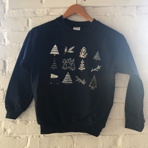 May include: A navy blue sweatshirt with a festive design featuring white and gold embroidered Christmas trees, branches, and a car.
