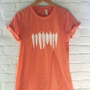 May include: A coral orange t-shirt with a white graphic of a row of carrots.