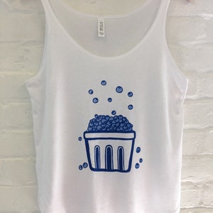 K&ouml;nnte beinhalten: Wei&szlig;es Tanktop mit einer blauen Illustration eines Korbes, der mit Blaubeeren &uuml;berquillt, und Blaubeeren, die um den Korb herum verstreut sind.