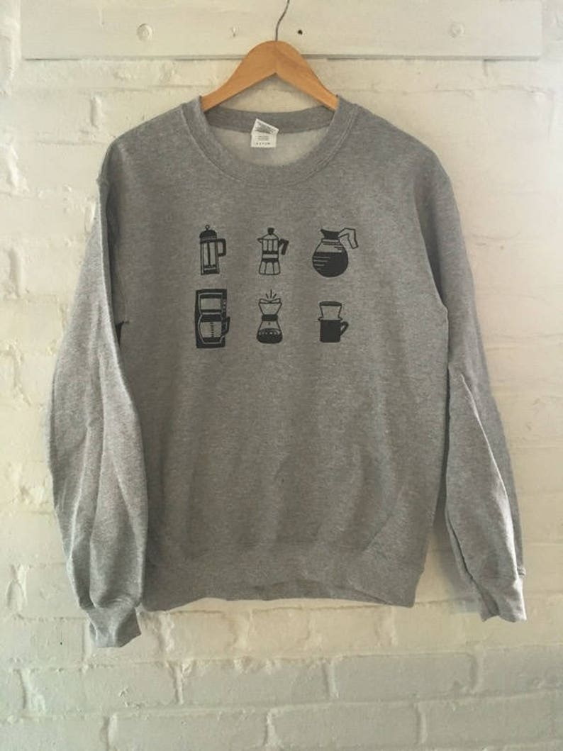 May include: Grey sweatshirt featuring a black graphic of various coffee brewing methods, including a French press, a percolator, a pour-over, and a coffee pot.